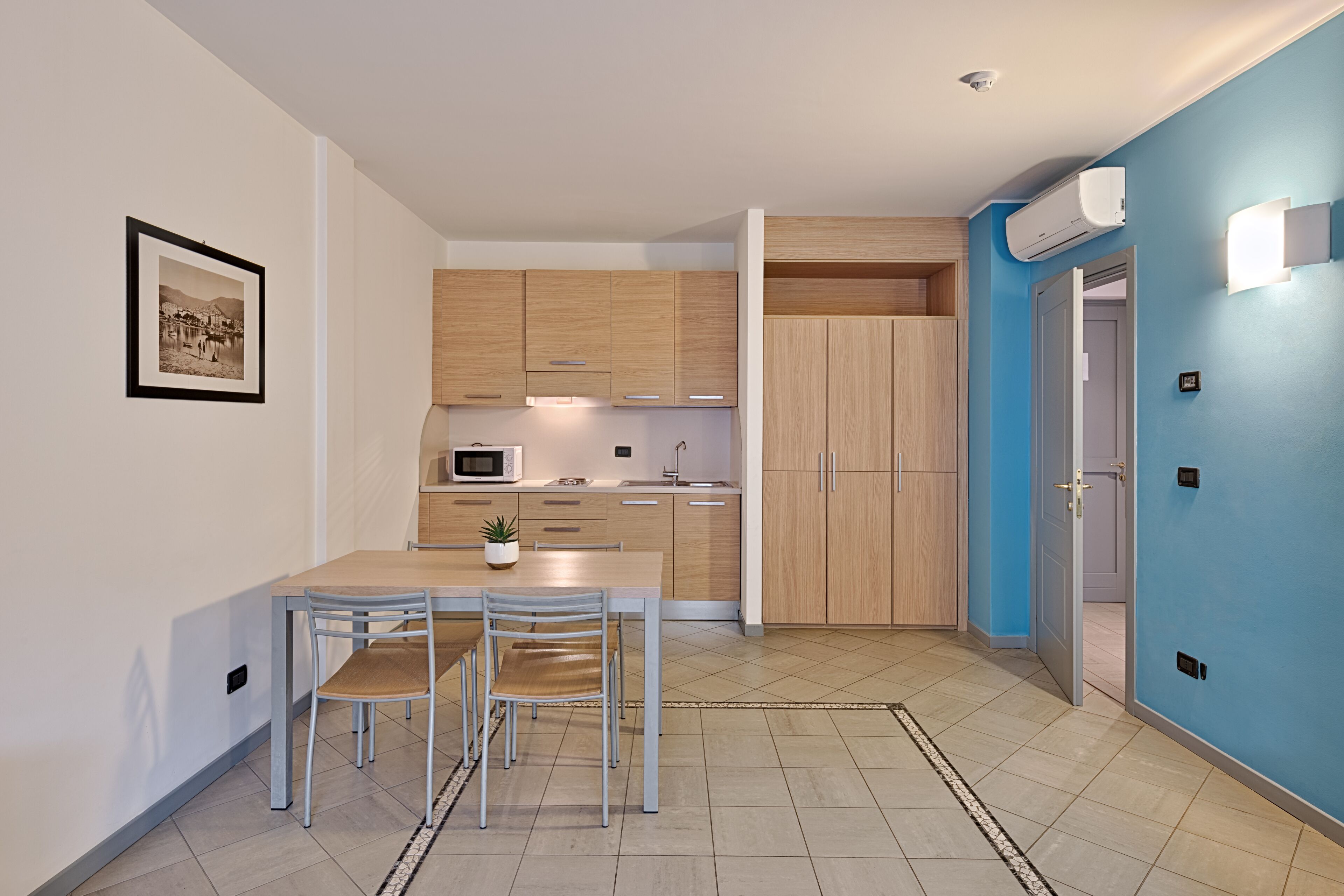Una cocina moderna con armarios de madera, una mesa de comedor con sillas, un microondas y una pequeña planta en maceta.