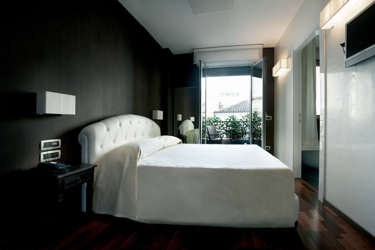 A modern hotel room with a large bed, bedside tables, a flat-screen TV, and a view of the outdoors.