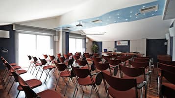 A conference room with rows of red chairs, a wooden floor, and a large window providing natural light.