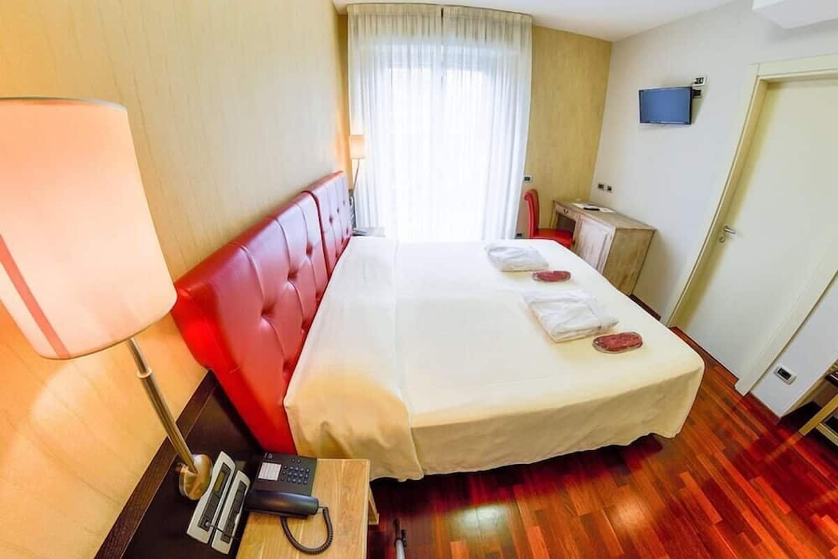 A hotel room with a bed, a bedside table with a lamp, a telephone, and a television on the wall.