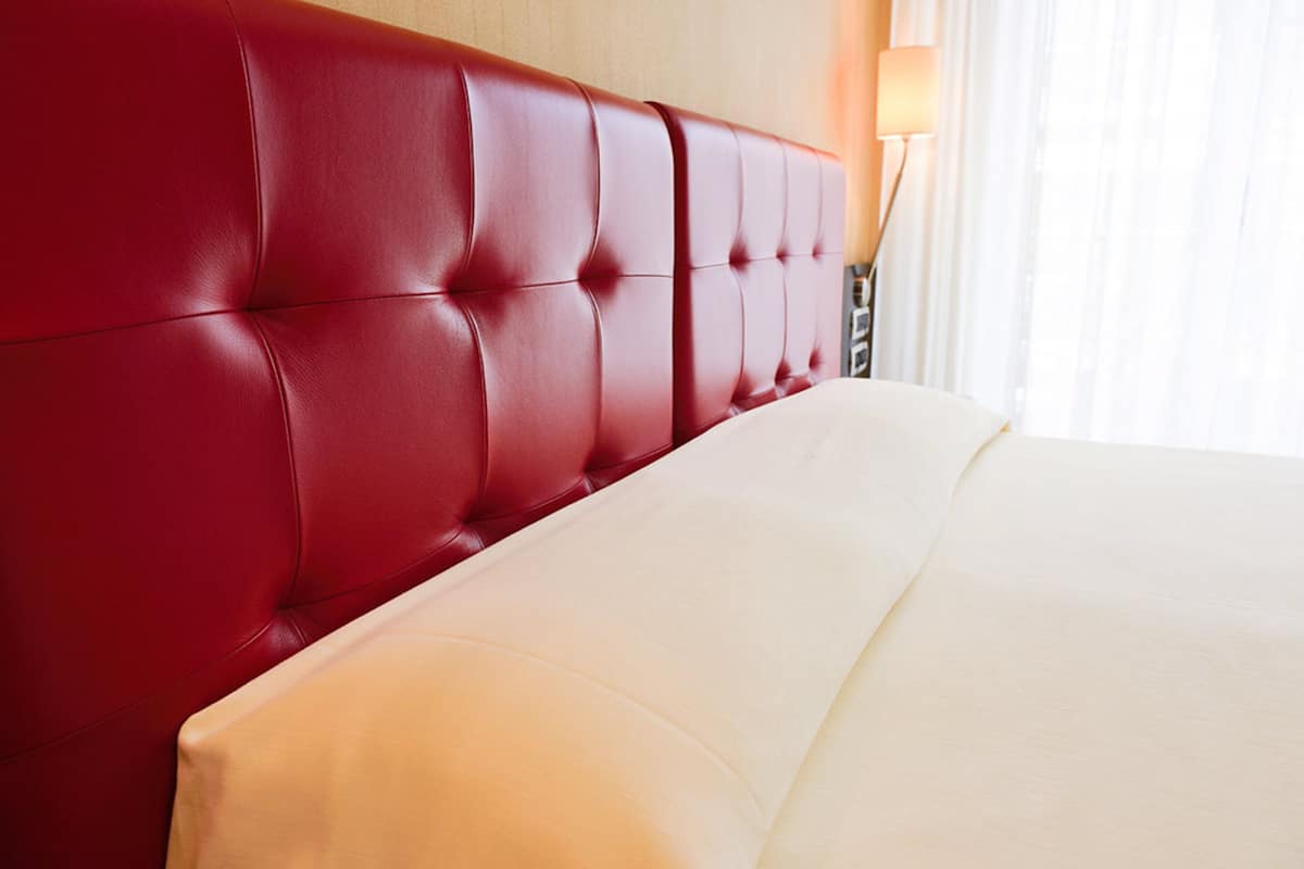 A hotel room with a red upholstered headboard and a white bedspread.