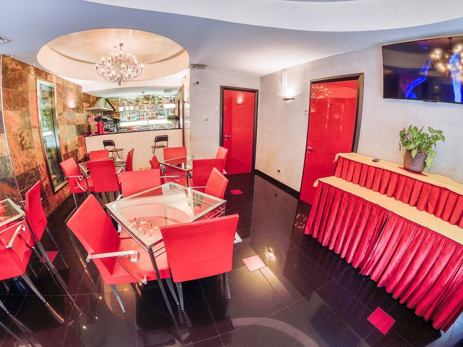 Un restaurant moderne avec des chaises rouges et une table en verre, un coin bar et un téléviseur fixé au mur.