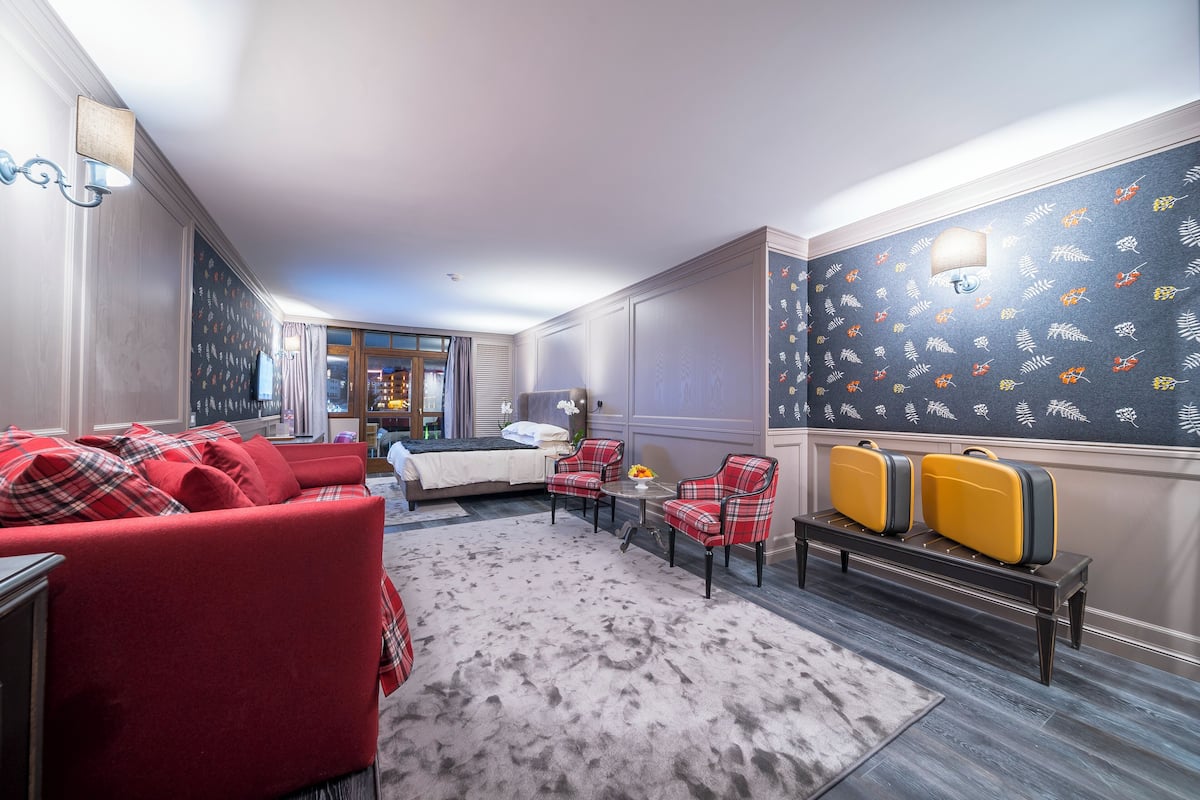 Ein Hotelzimmer mit einem roten Sofa, einem kleinen Tisch, einer Bank mit Gepäck und einer Wand mit Muster.