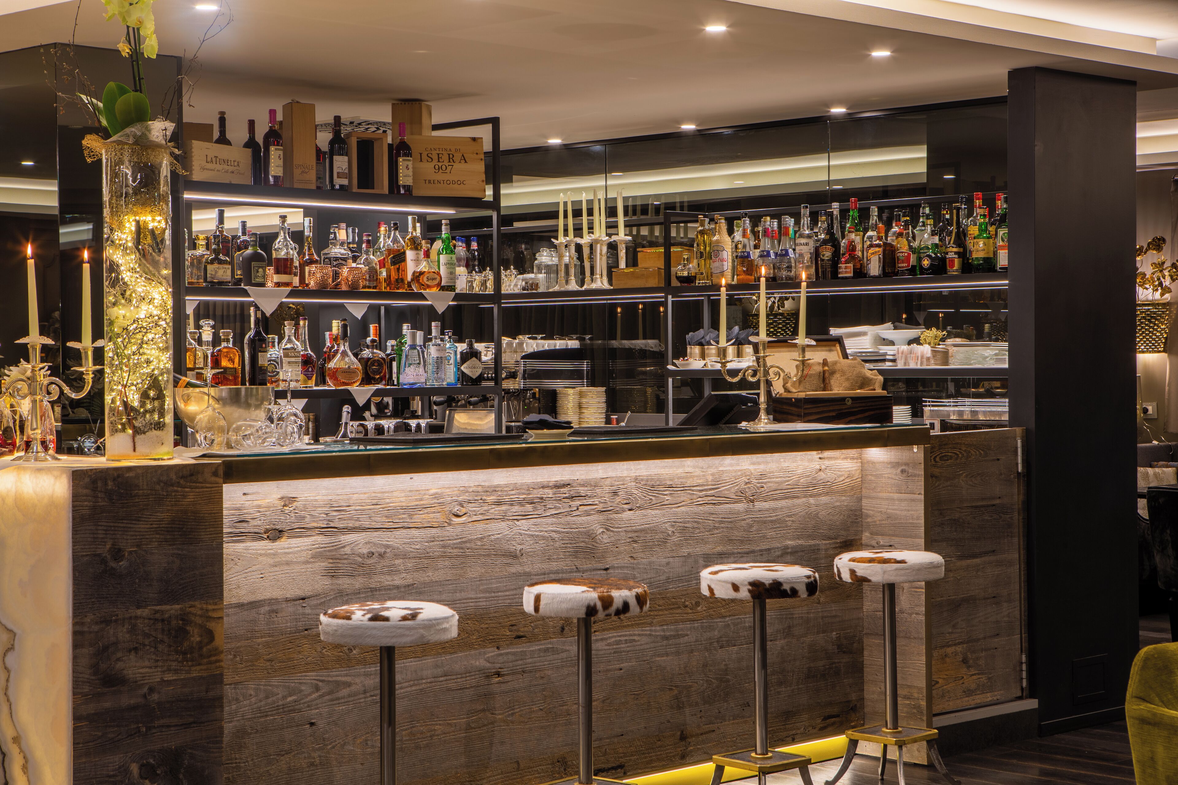 A bar area with wooden bar counter, multiple liquor bottles, and stools.