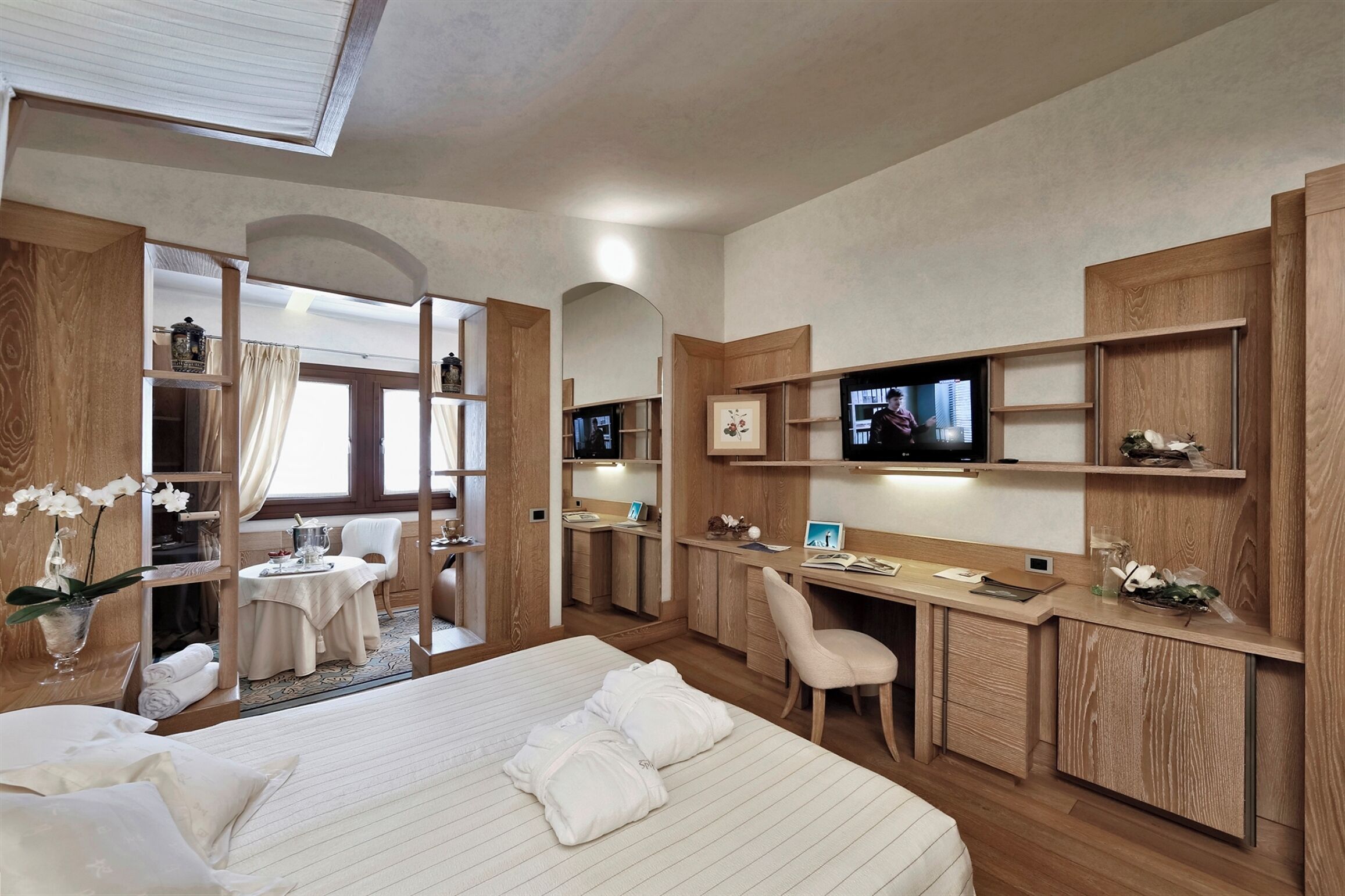 A hotel room with a bed, a desk, a television, and a bathroom visible through an open door.