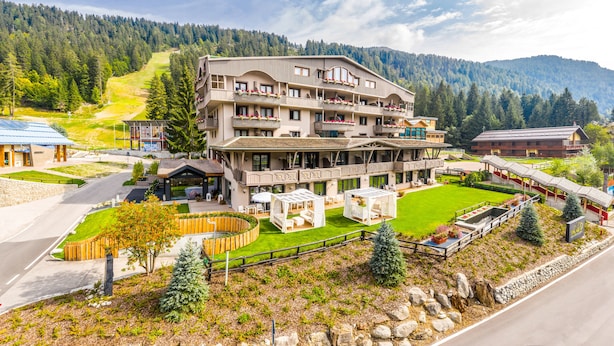 Un hotel de varios pisos con balcones, un patio central y montañas al fondo.