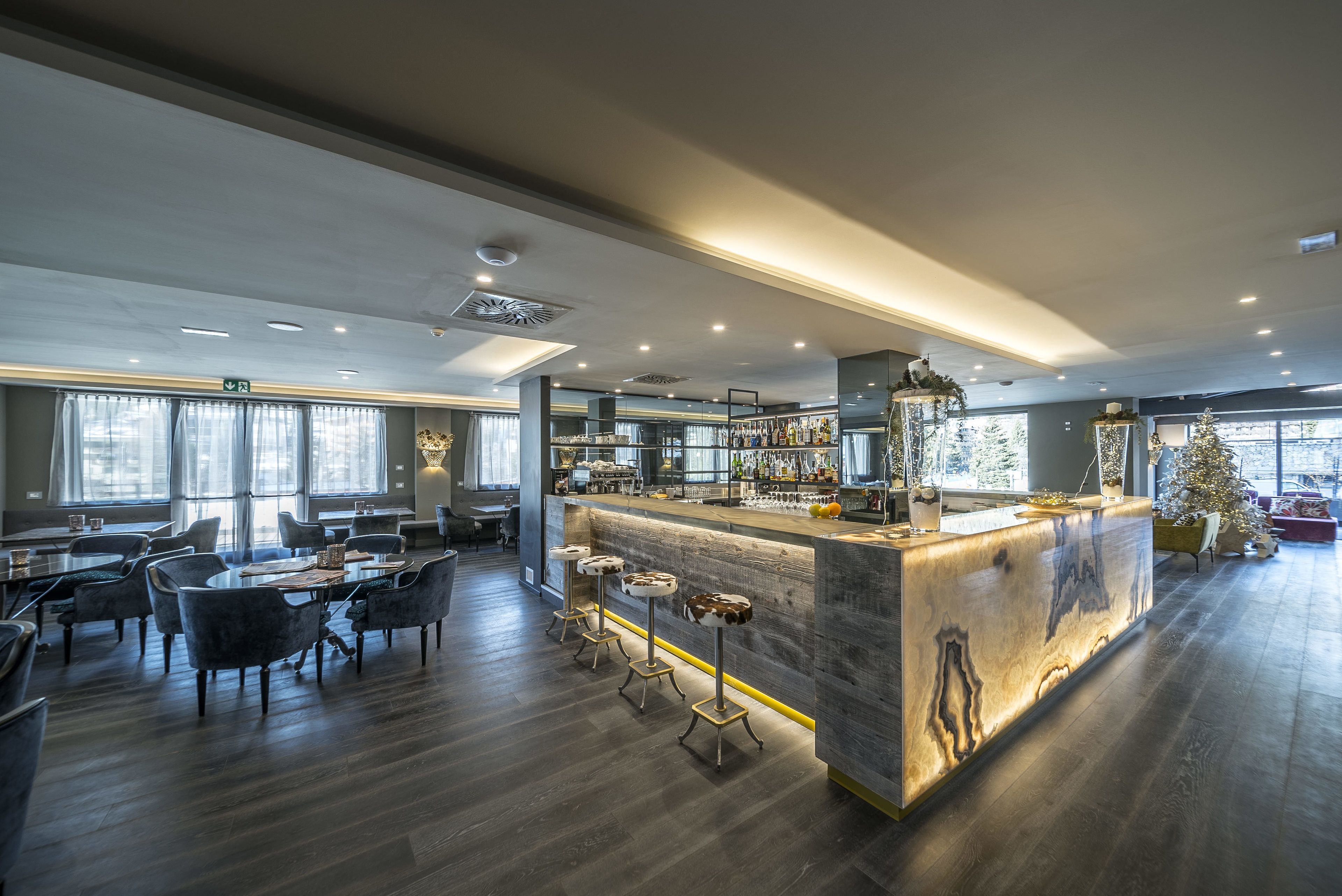 A modern bar area with a wooden bar counter, bar stools, and a seating area with tables and chairs.