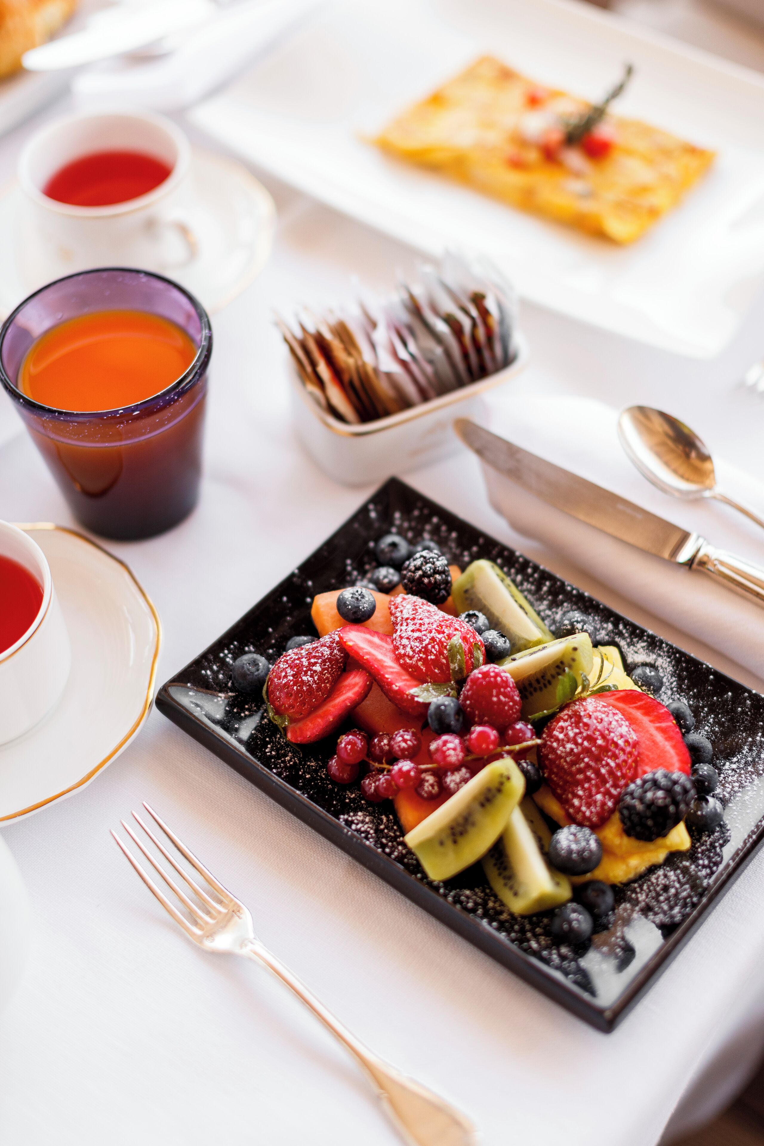 A breakfast setting with a fruit platter, coffee cups, and a dessert plate.