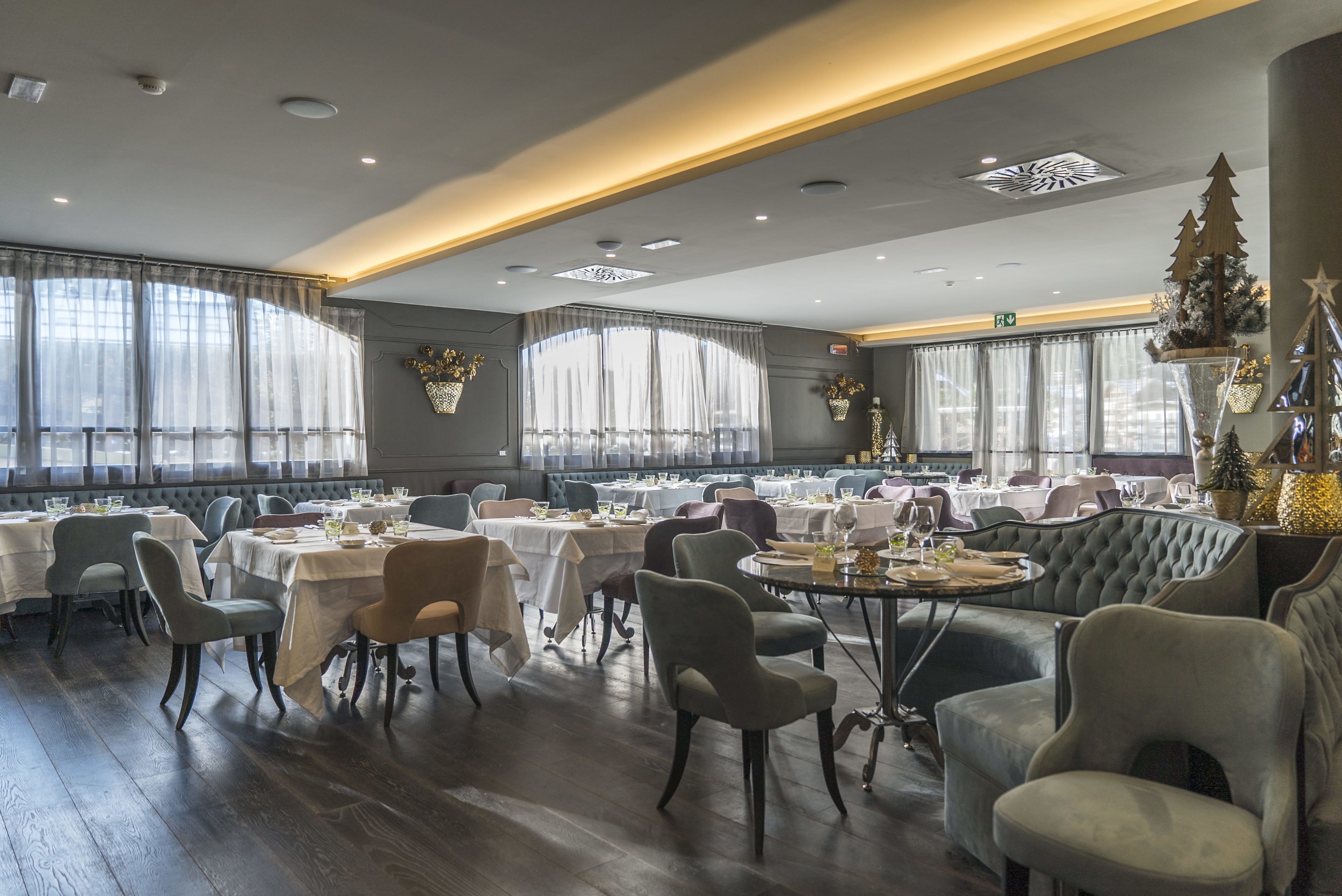 A spacious dining area with multiple tables and chairs, large windows with sheer curtains, and a modern ceiling design.