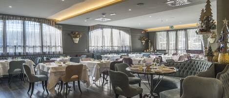 A spacious dining area with multiple tables and chairs, large windows with sheer curtains, and a modern ceiling design.
