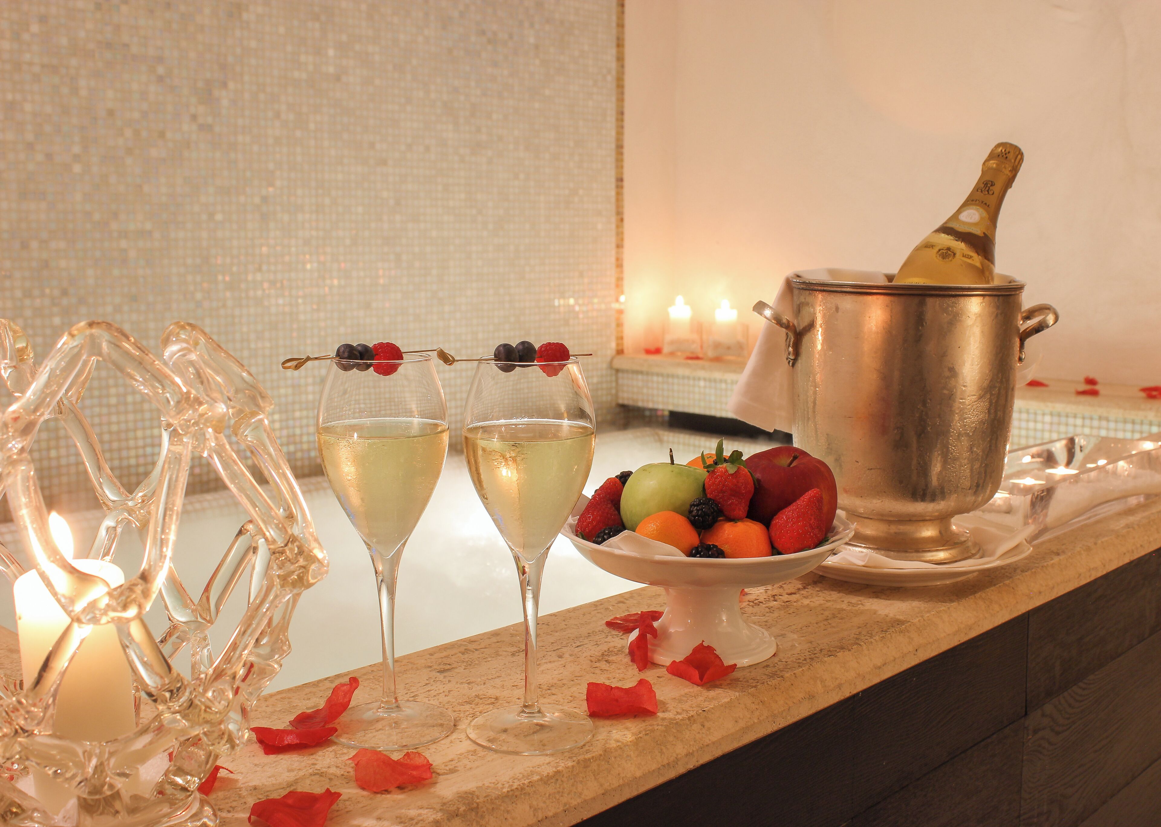 Deux flûtes à champagne décorées de fruits, un seau en métal et un saladier rempli de fruits, le tout posé sur le comptoir d’un bar.