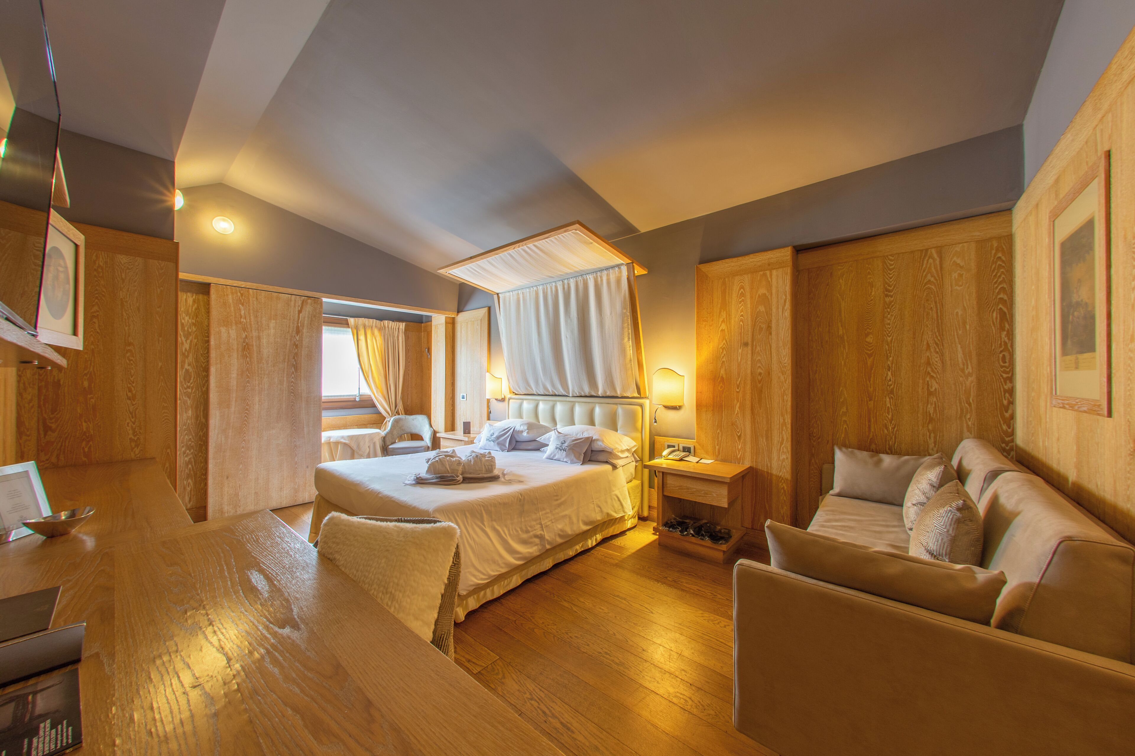 A hotel room with a bed, a sofa, a desk, and a bedside table.