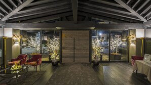 Un interior moderno con techo de madera, dos árboles en macetas con luces, sillas rojas y una mesa.