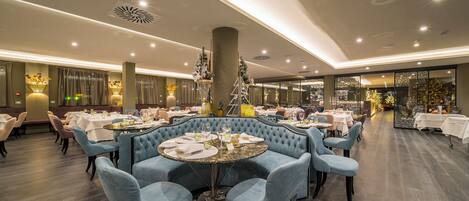 Un restaurante con mesas redondas, sillas tapizadas en azul y una columna central.