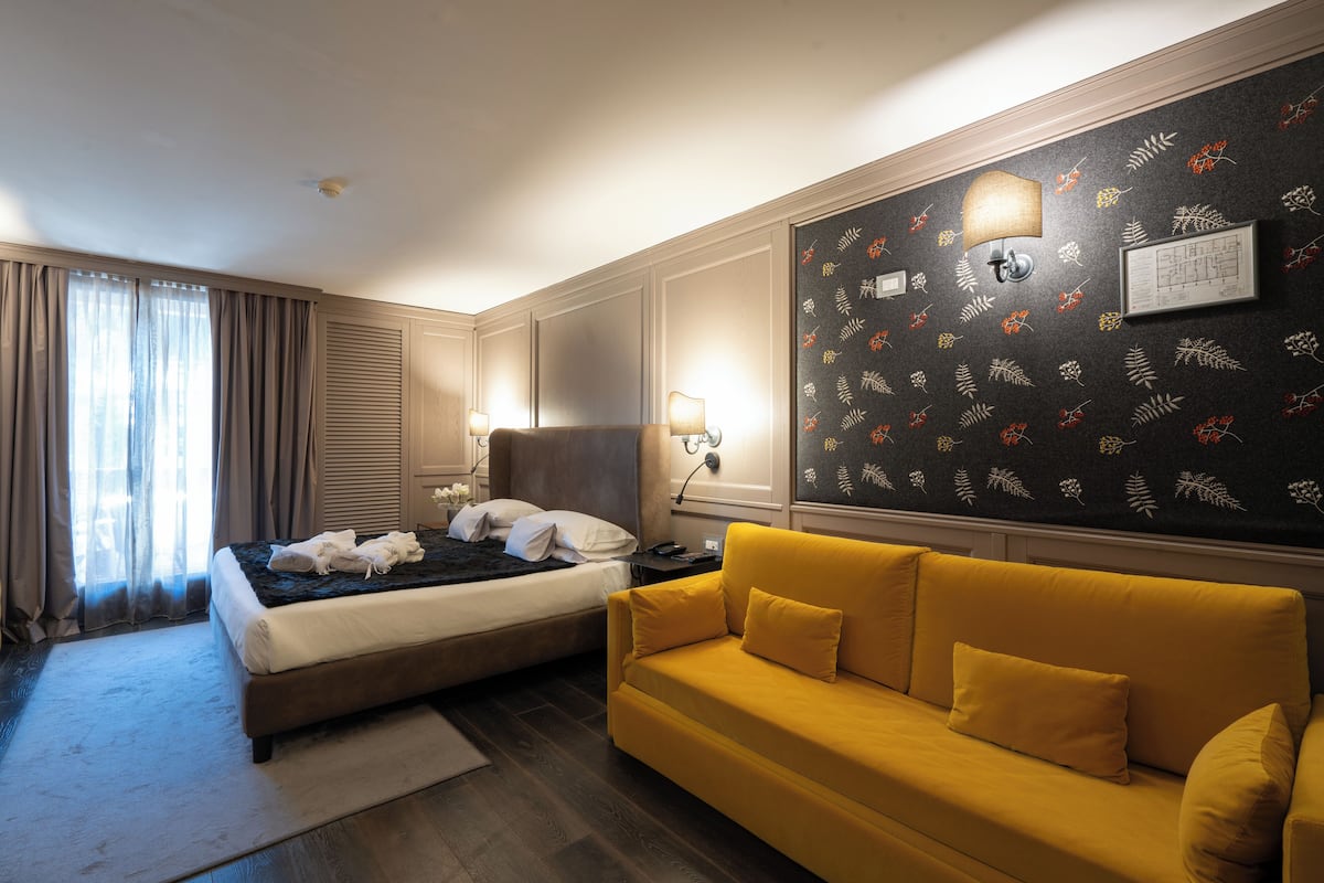 Ein Hotelzimmer mit einem Bett, einem gelben Sofa, einer Wand mit floralem Muster und einer Deckenleuchte.