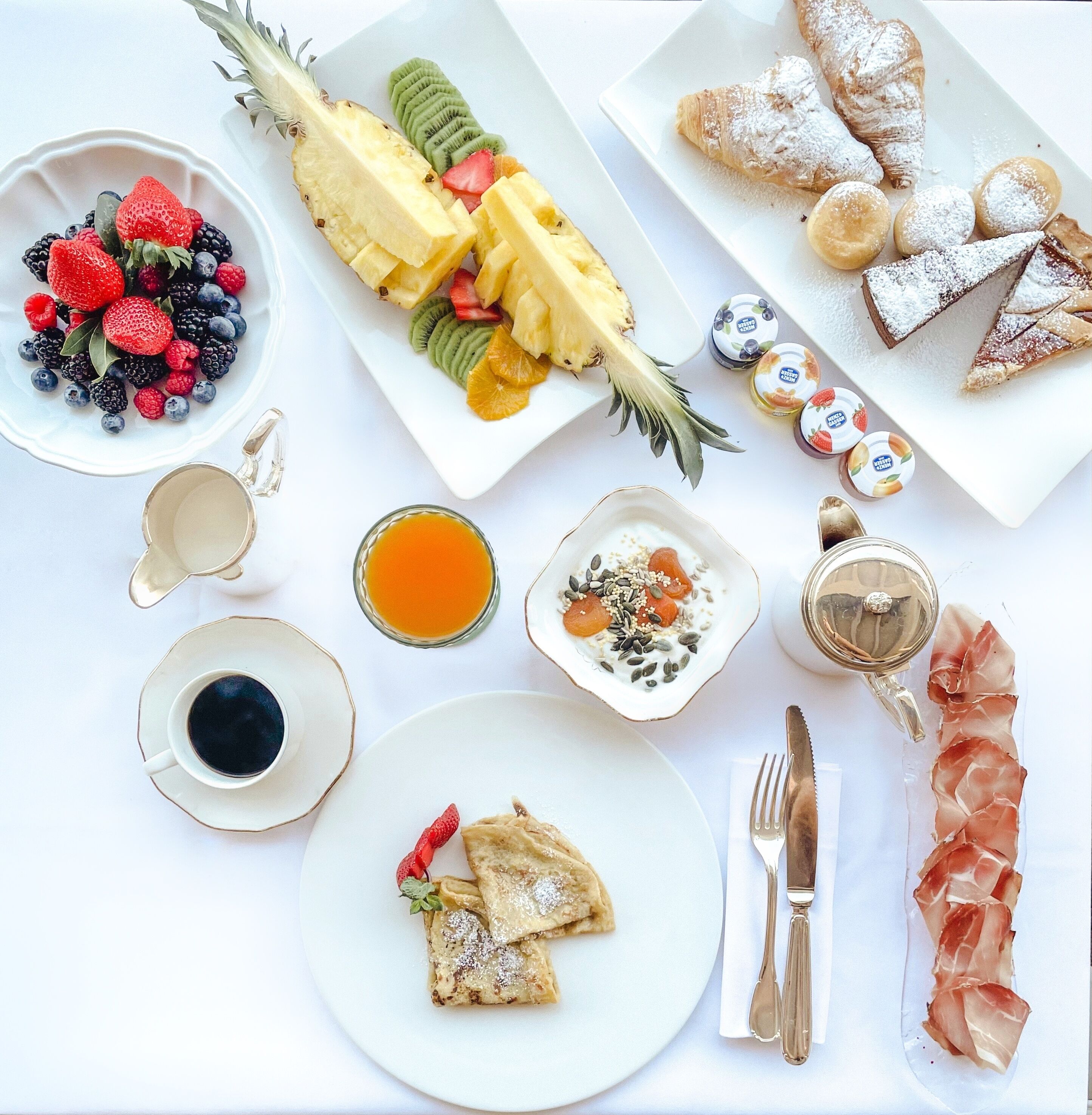 A breakfast spread with various fruits, pastries, and beverages on a white table.