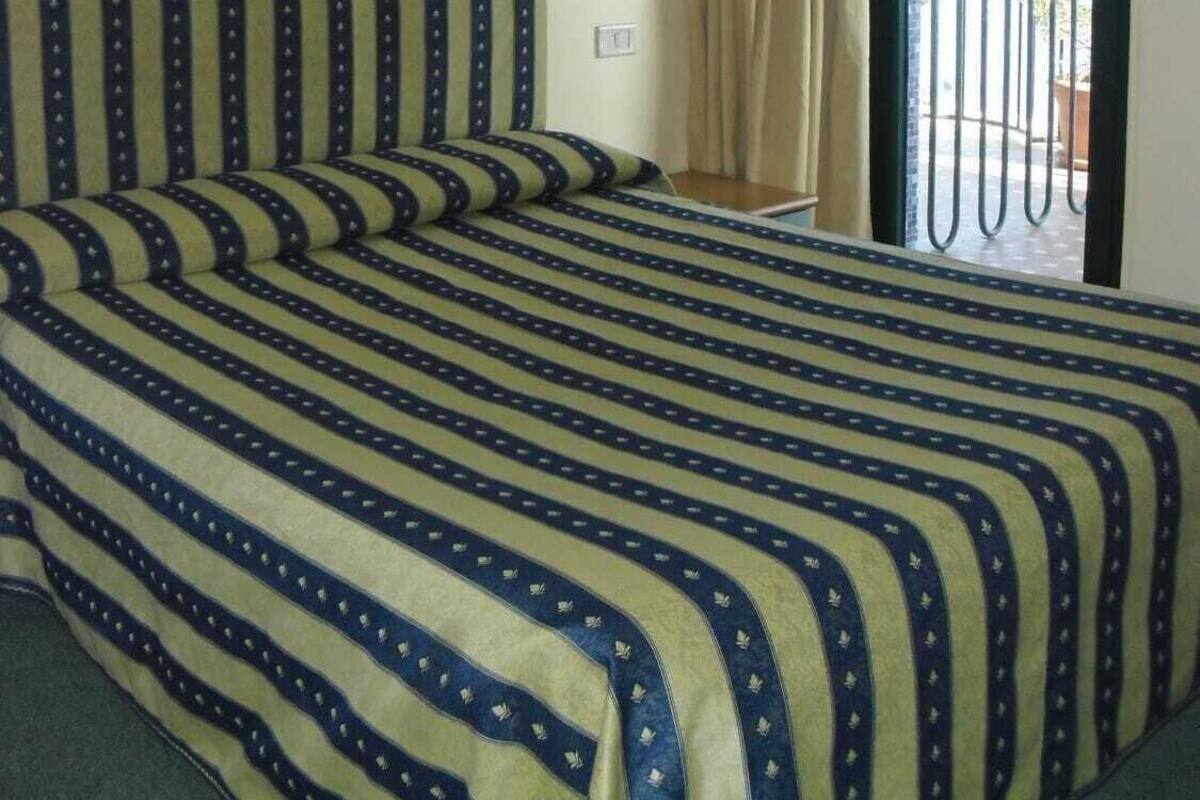 A hotel room with a bed, a window with curtains, and four framed pictures on the wall.