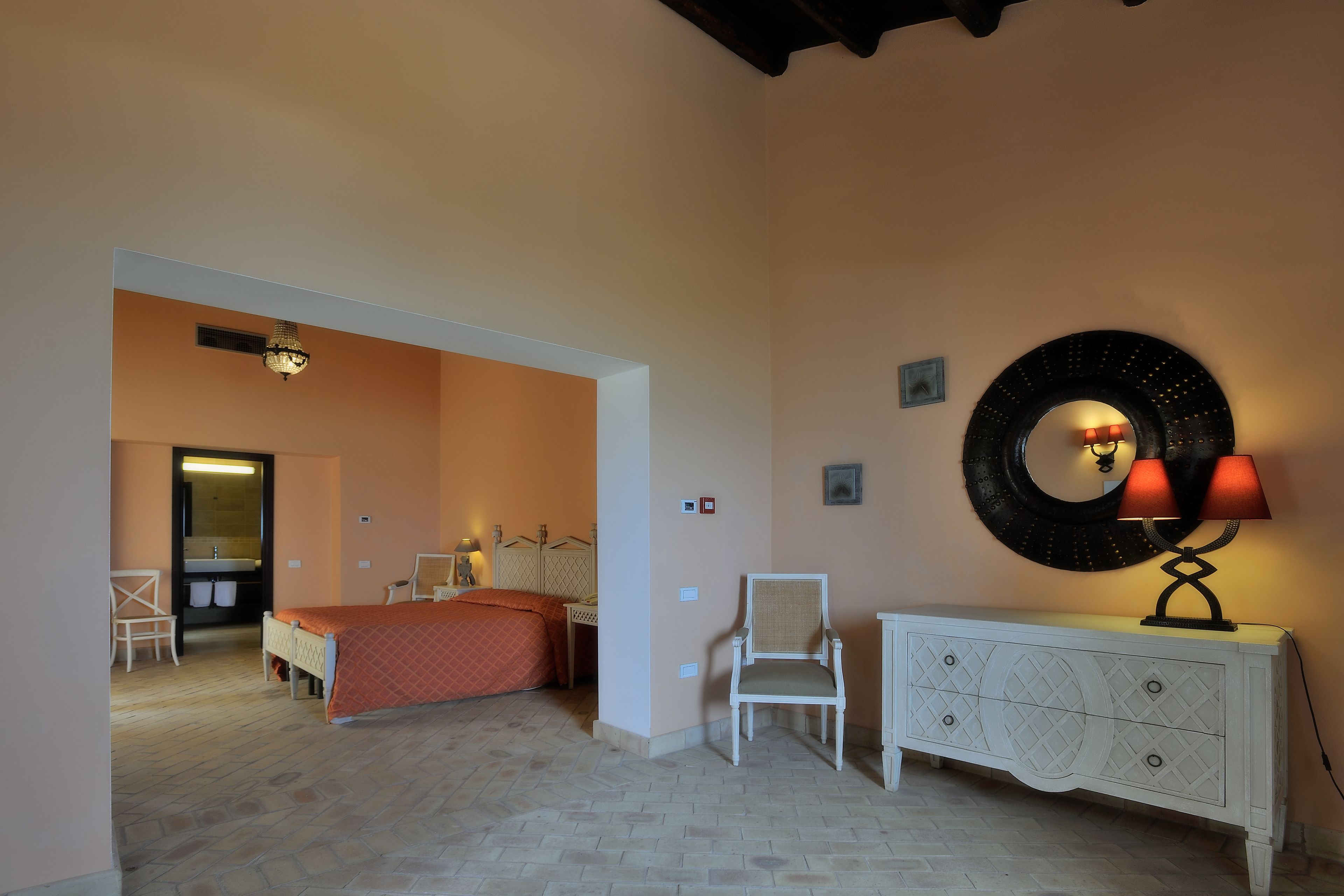 Ein Schlafzimmer mit einem Bett, einem Sessel, einem Schminktisch und einer Wandleuchte.