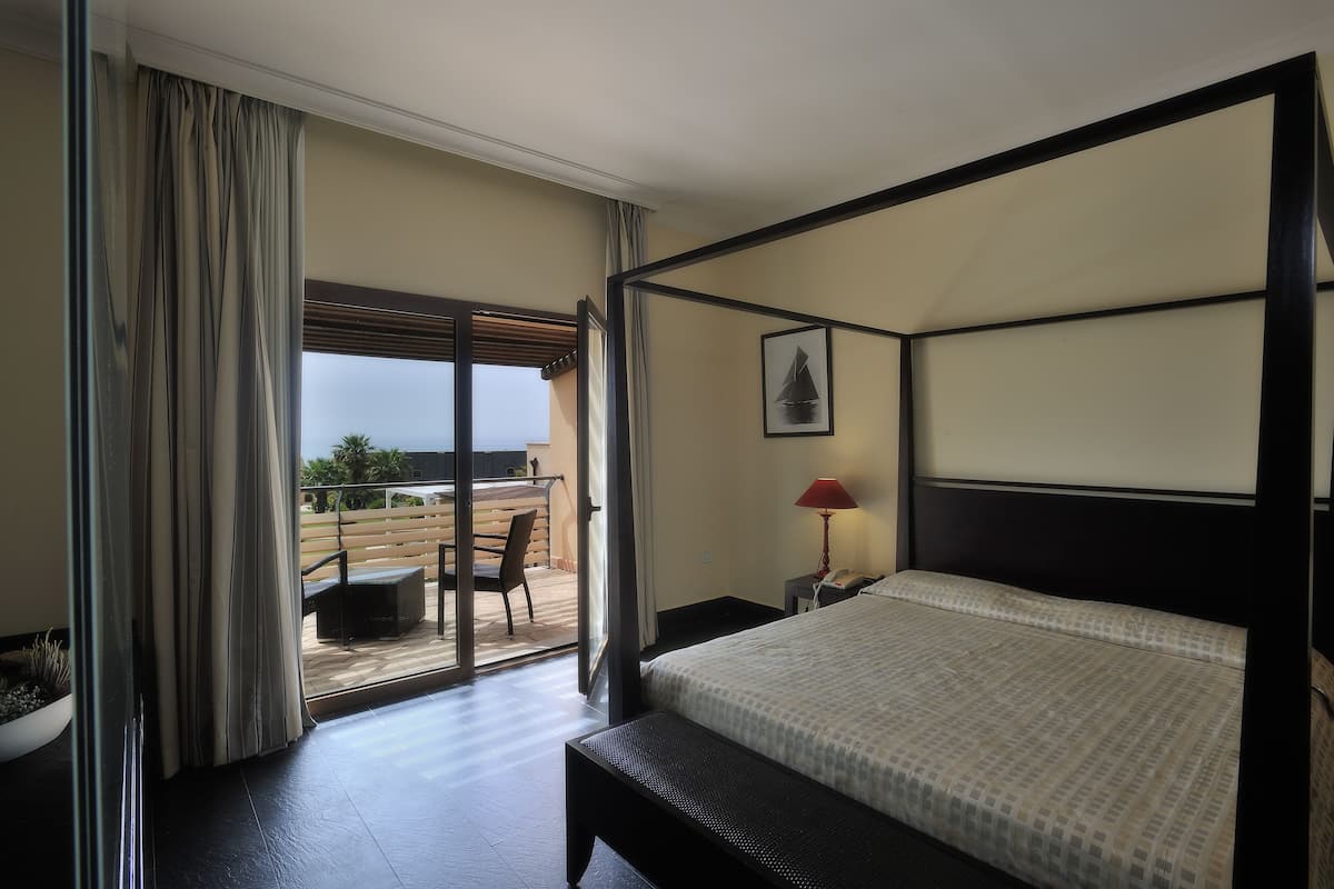 A four-poster bed in a hotel room with a view to the outside.