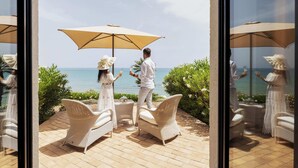 A couple seated at a table with a large umbrella, overlooking a scenic ocean view. - Falconara Greenblu Resort (Butera)