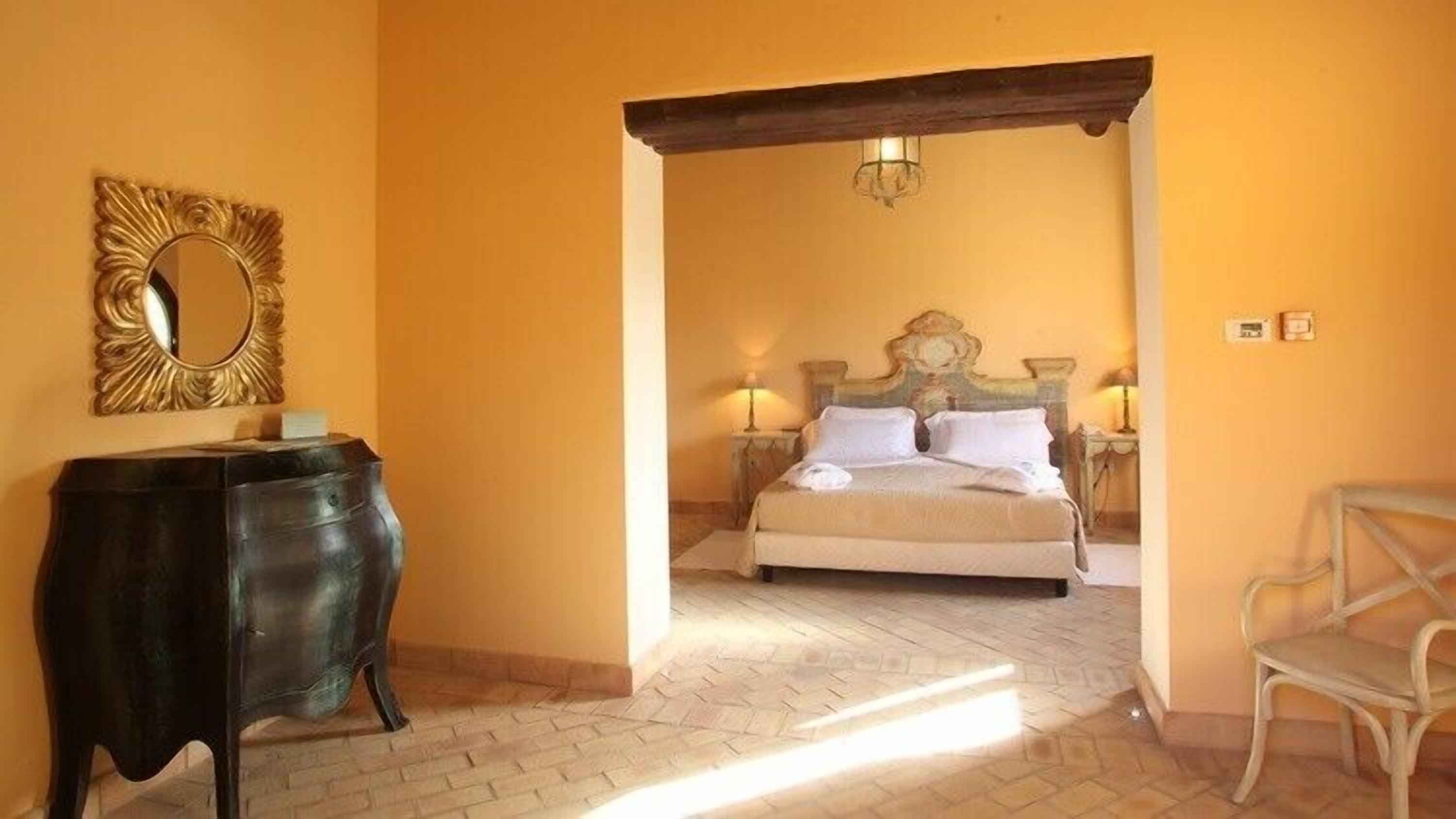 A bedroom with a bed, a nightstand, a lamp, a chair, and a decorative mirror.