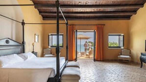 A bedroom with a four-poster bed, two chairs, a wooden ceiling, and a view of the sea through open curtains. - Falconara Greenblu Resort (Butera)