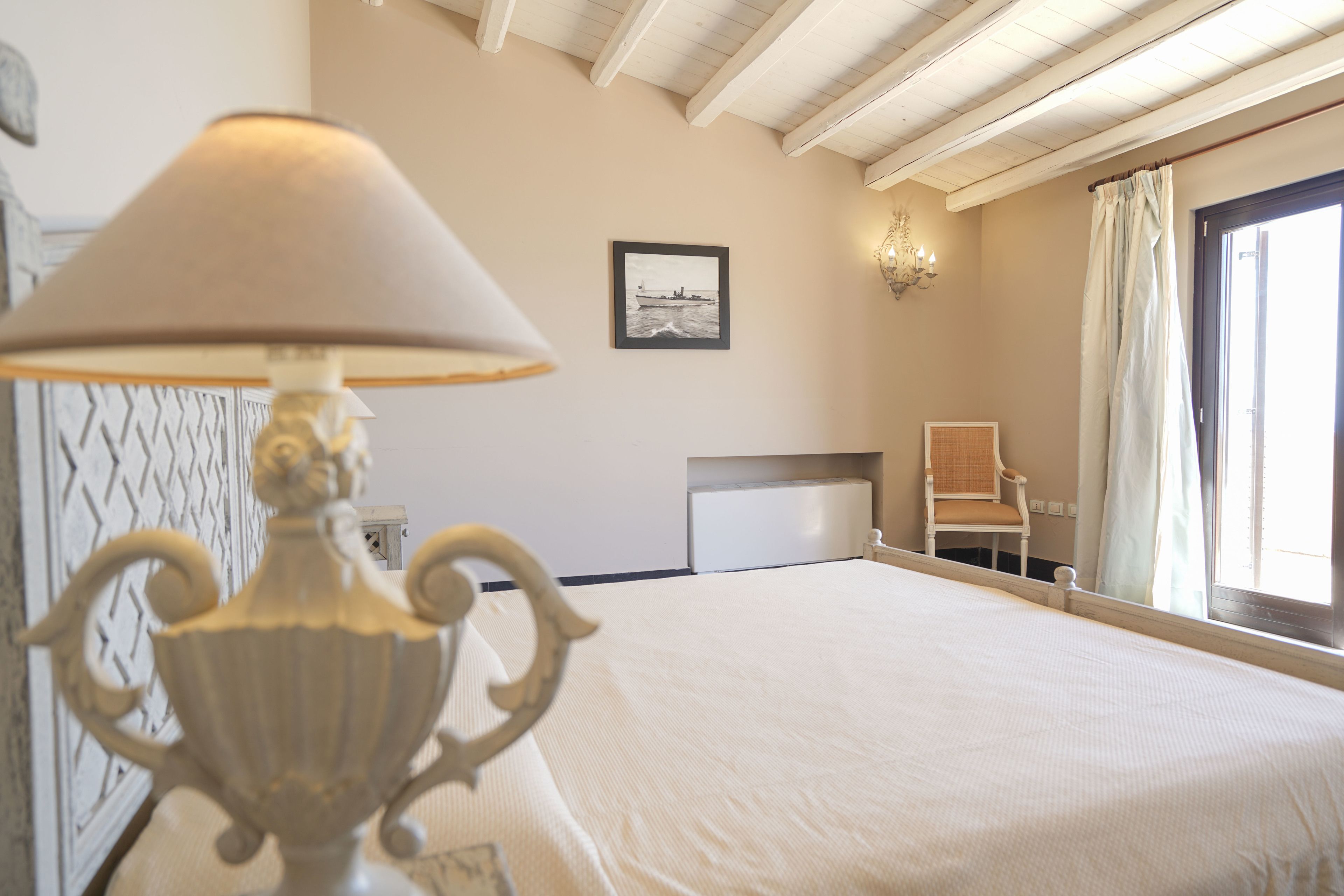 A hotel room with a bed, a lamp, a picture on the wall, a chair, and a window with curtains.