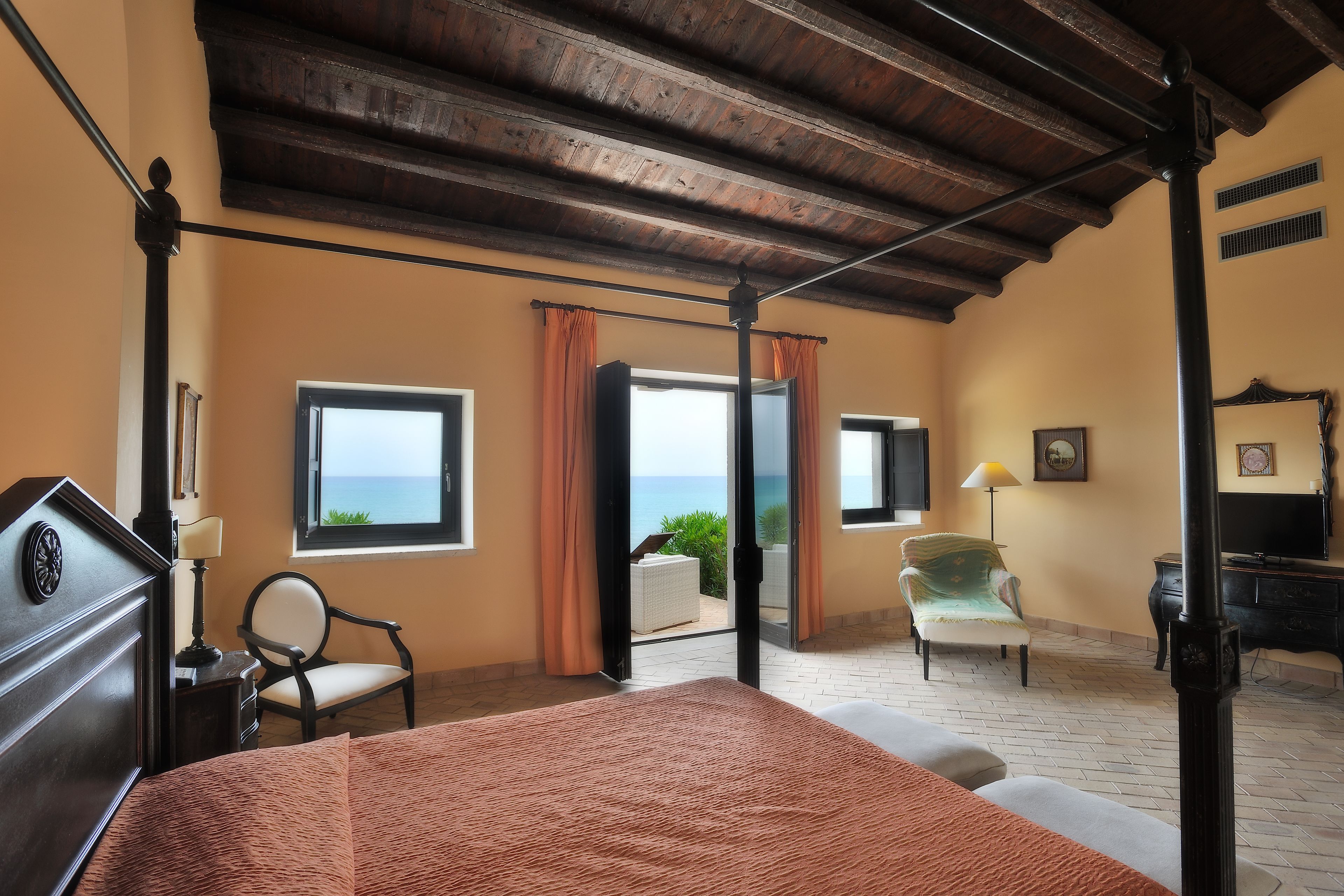 Un dormitorio con una cama grande, una silla, un escritorio y vista al mar a través de una ventana.