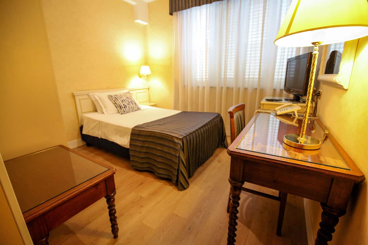 Una habitación de hotel con cama, mesita de noche, escritorio, lámpara y televisión.