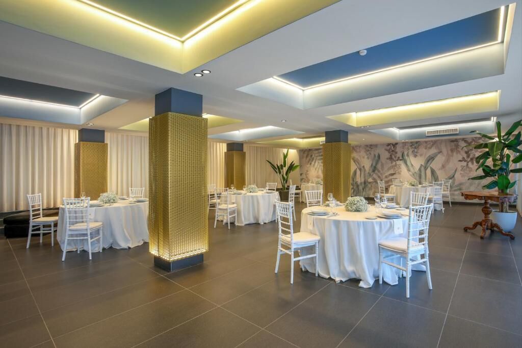 A spacious banquet hall with round tables and white chairs, featuring recessed lighting and a decorative column.