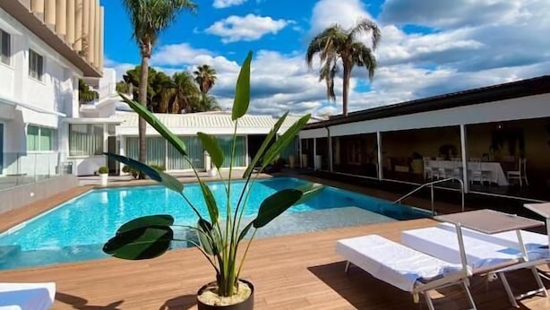 A poolside area with a clear blue sky, palm trees, and a modern building with a unique facade. - Hotel I Gigli (Nola)