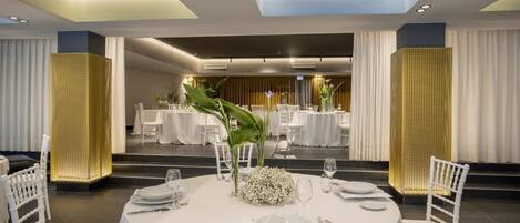 Un espace repas avec des tables rondes disposées pour accueillir quatre personnes, des chaises blanches et un arrangement floral central.