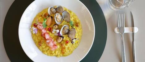 A plate of food with clams and shrimp on a white plate, accompanied by a fork and knife on a green mat.