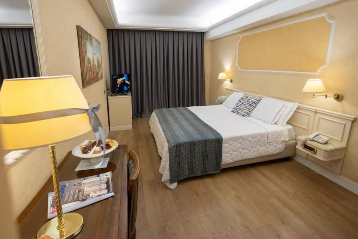 Habitación de hotel con cama, lámparas de noche, televisor, escritorio con lámpara y una revista en el suelo.