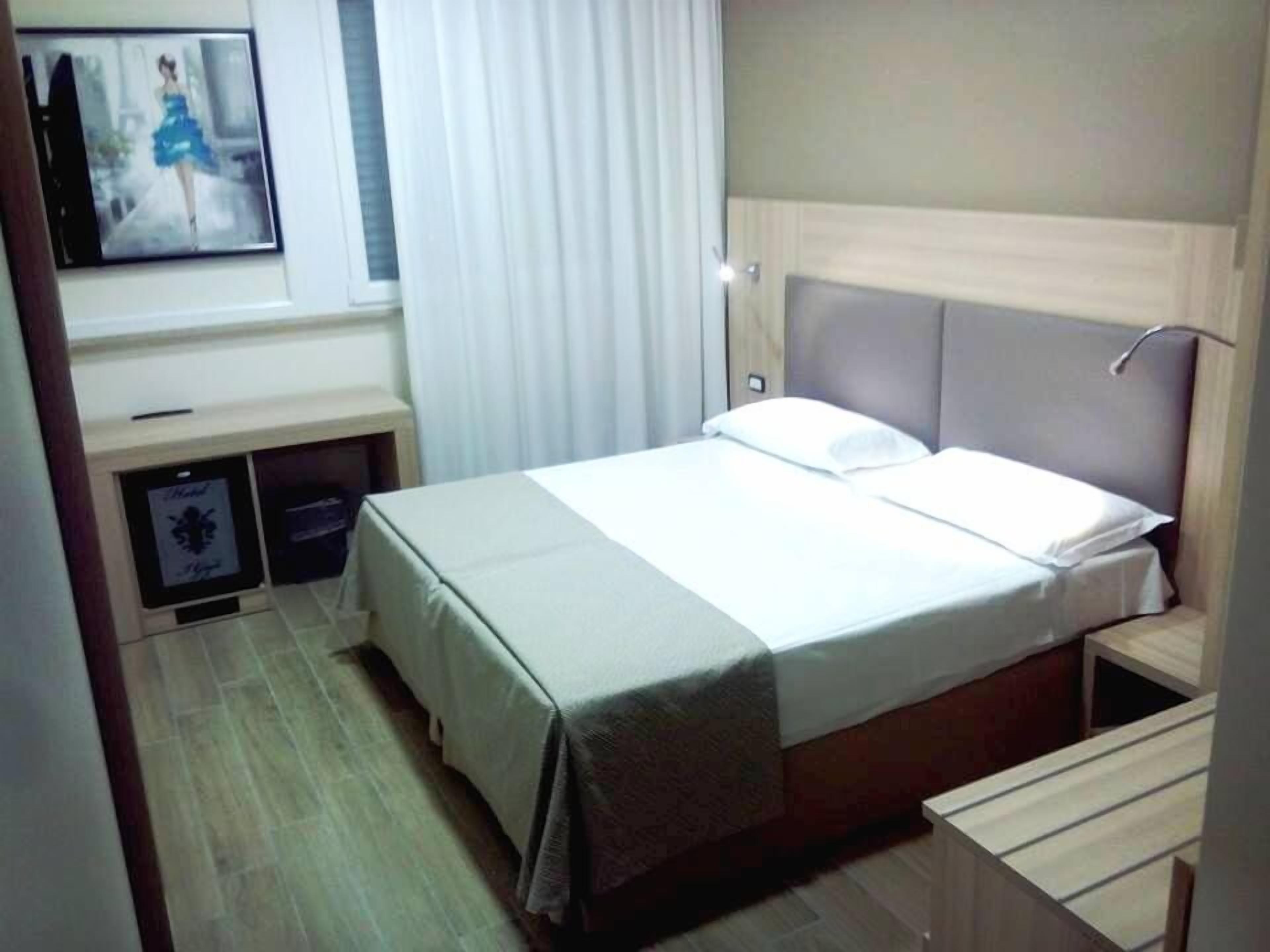 A hotel room with a bed, bedside tables, a desk, and a television.