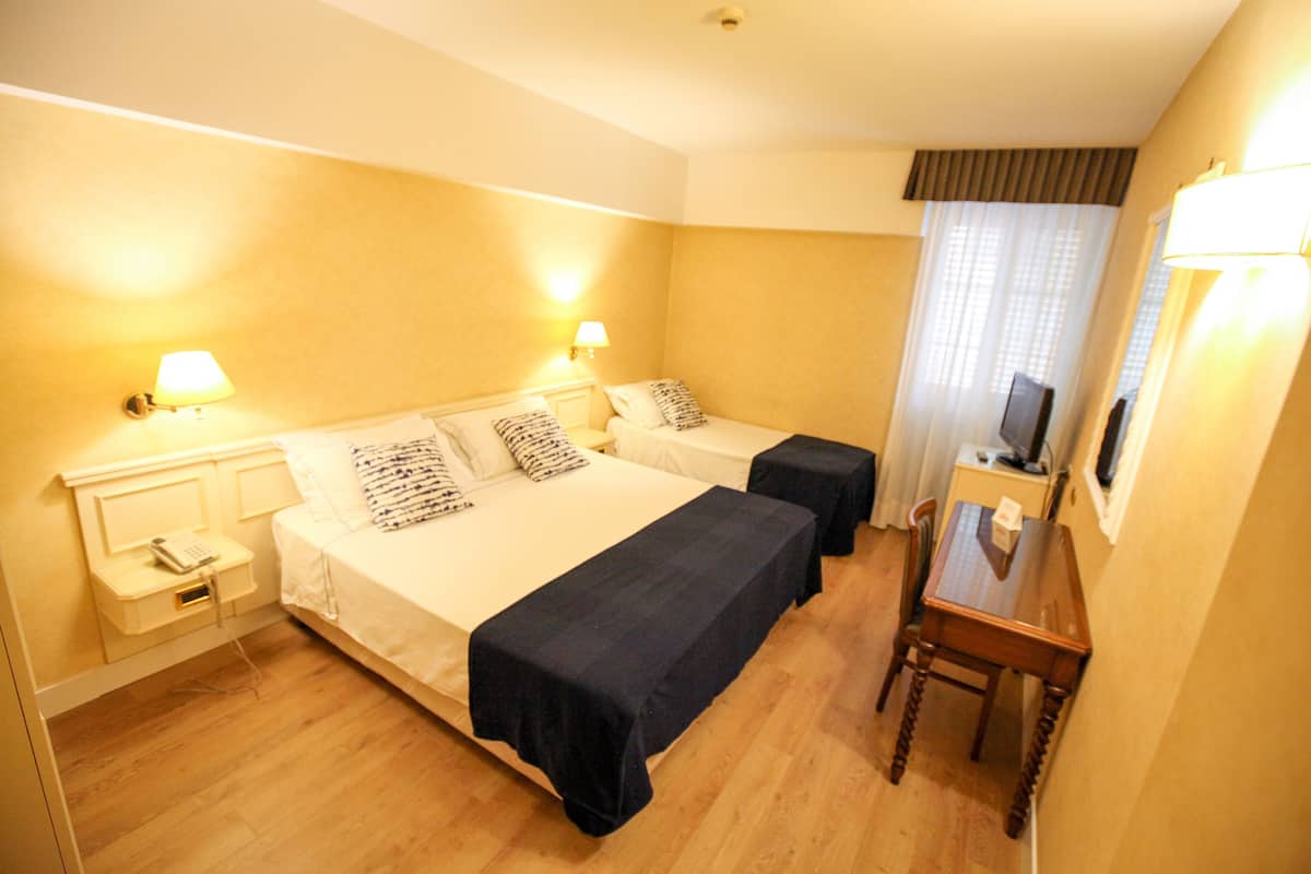 Habitación de hotel con dos camas, mesitas de noche, un escritorio y una silla.