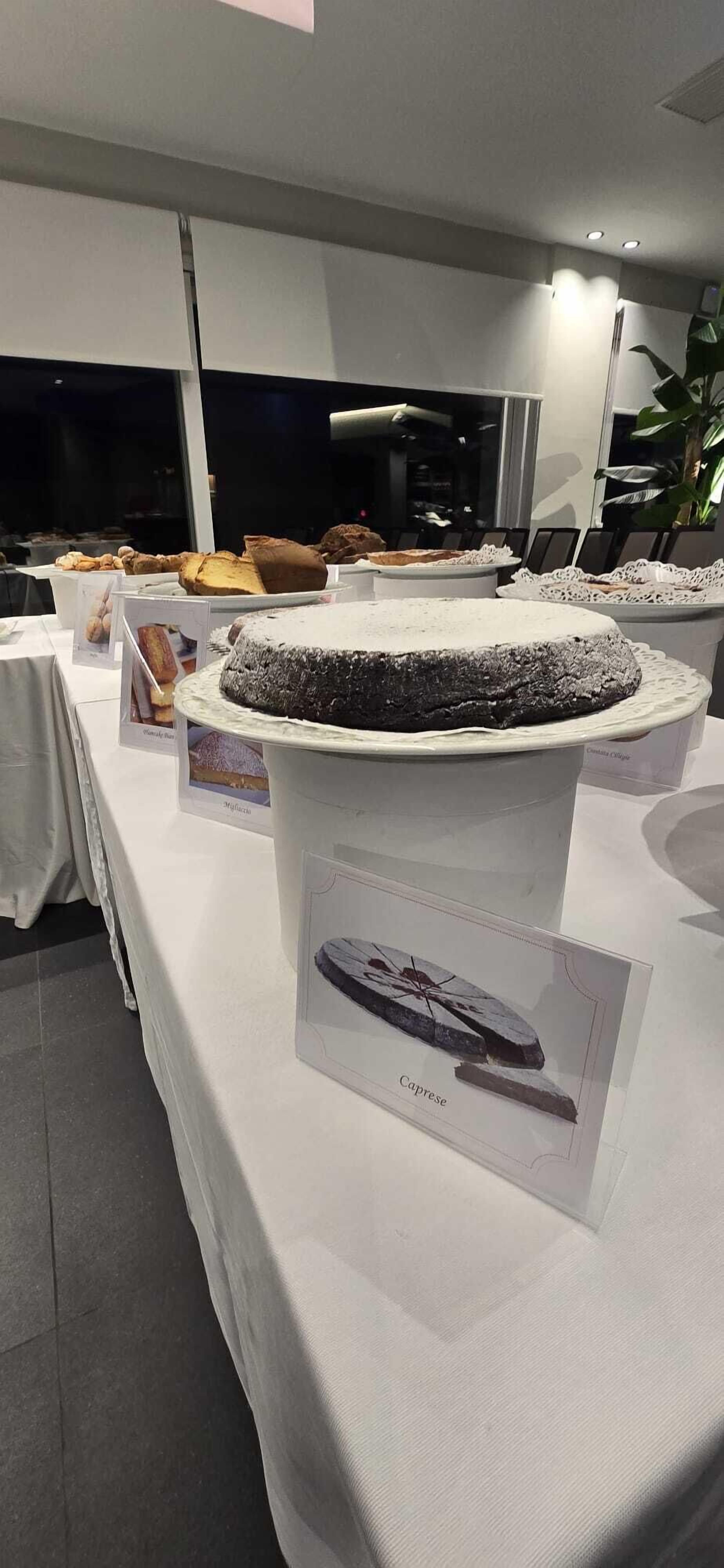 A dessert display with various cakes and pastries, a white tablecloth, and a framed picture of a ship labeled "Cargue".