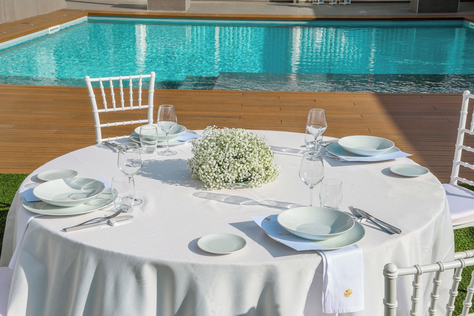 Mesa redonda dispuesta para una comida, con una piscina al fondo.