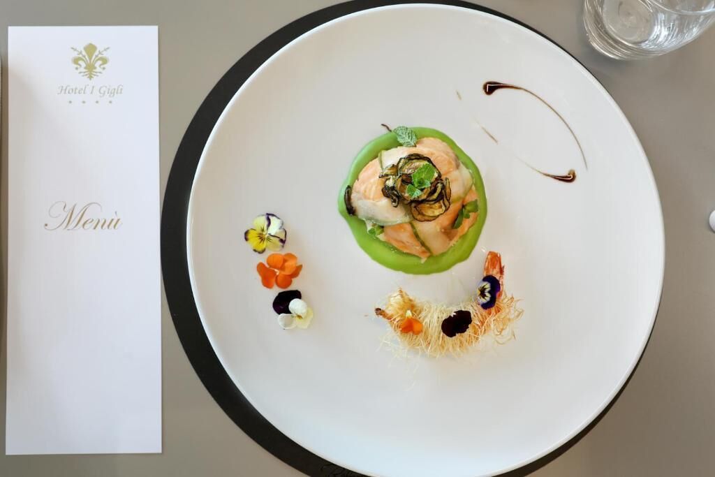 Un plato blanco con salsa verde, salmón y adornos sobre una mesa con un menú y un vaso de agua.