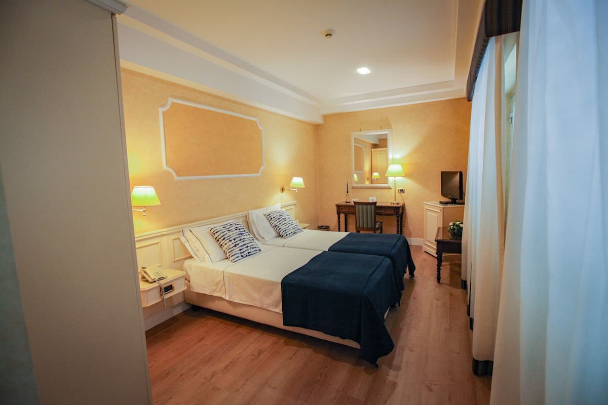 Habitación de hotel con cama, lámparas de noche, escritorio con silla, espejo y televisión.