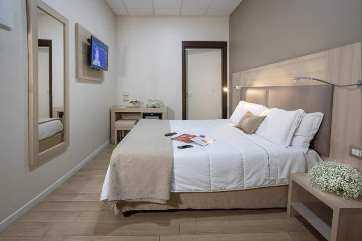 Un dormitorio con cama, mesita de noche y televisor montado en la pared.