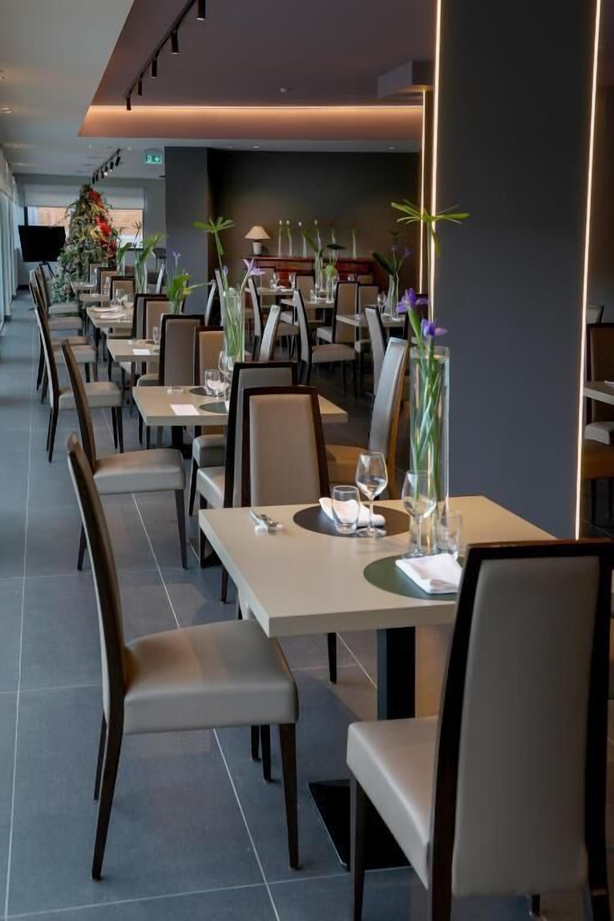 Un restaurant moderne avec de longues tables et des chaises, chacune agrémentée d’un vase de fleurs.