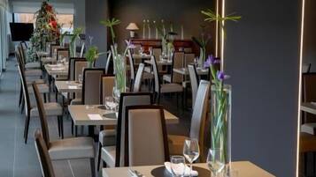 Un restaurante moderno con mesas y sillas largas, cada una con un jarrón de flores.