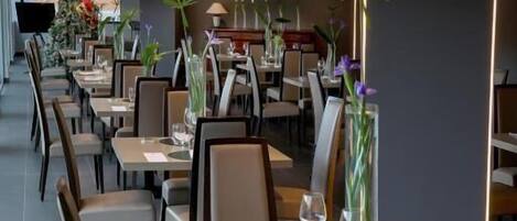 Un restaurant moderne avec de longues tables et des chaises, chacune agrémentée d’un vase de fleurs.
