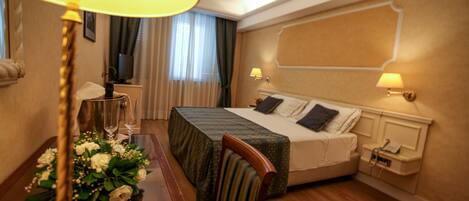 A hotel room with a bed, bedside lamps, a table with a vase of flowers, a chair, and a window with curtains.
