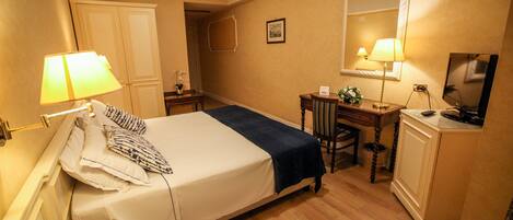 A hotel room with a bed, bedside lamps, a desk with a chair, a mirror, and a television.