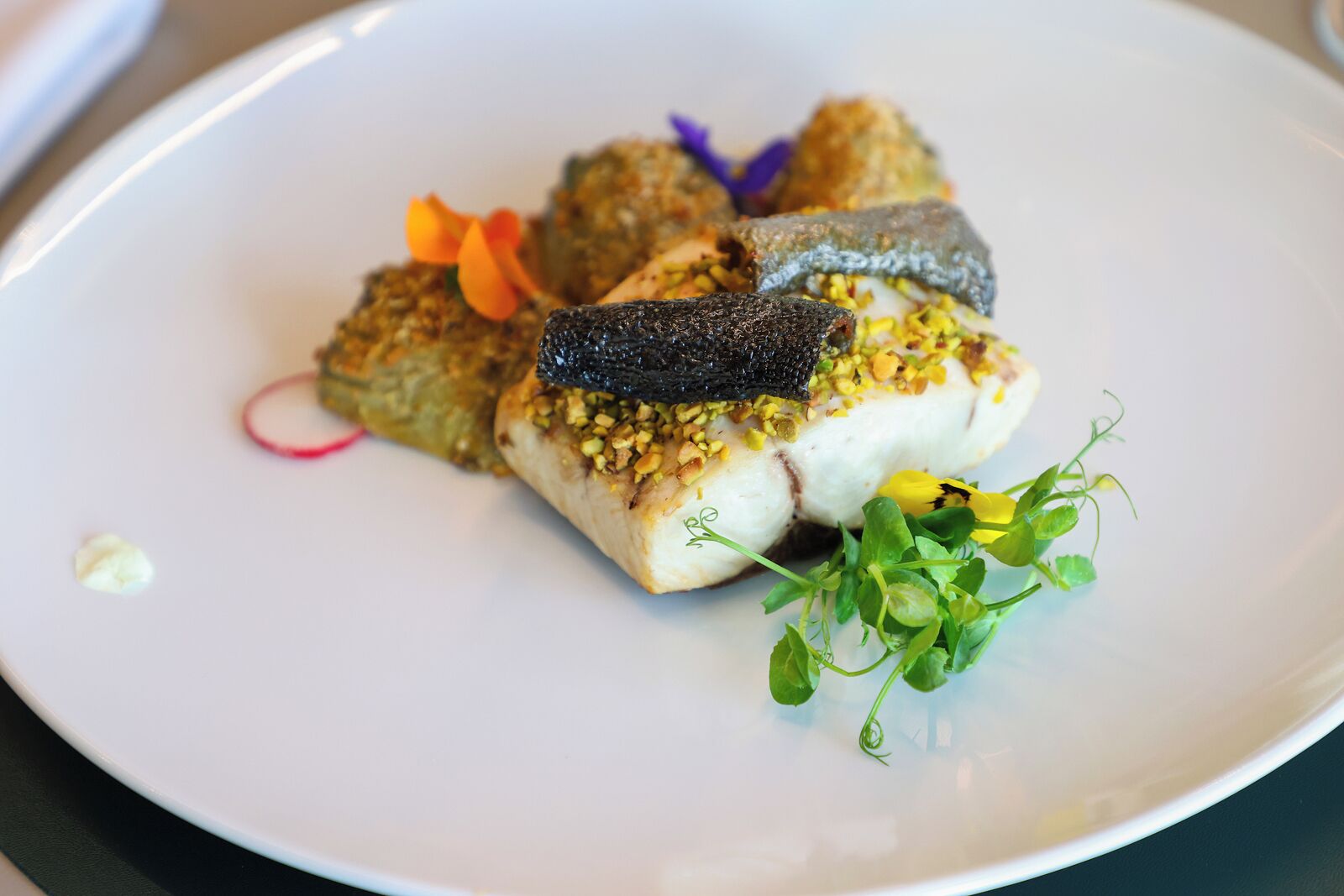 A white plate with a fish dish, green garnish, and a small flower.