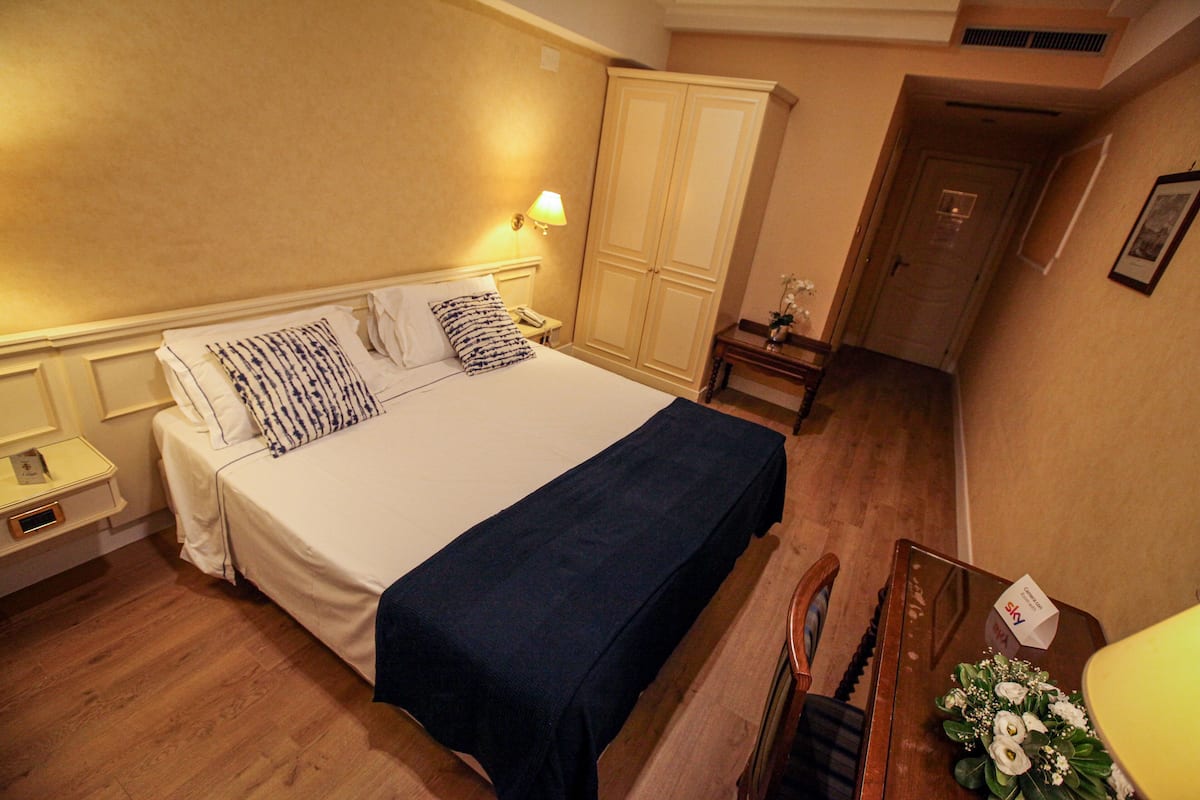 Una habitación de hotel con cama, mesitas de noche, armario, escritorio y silla.