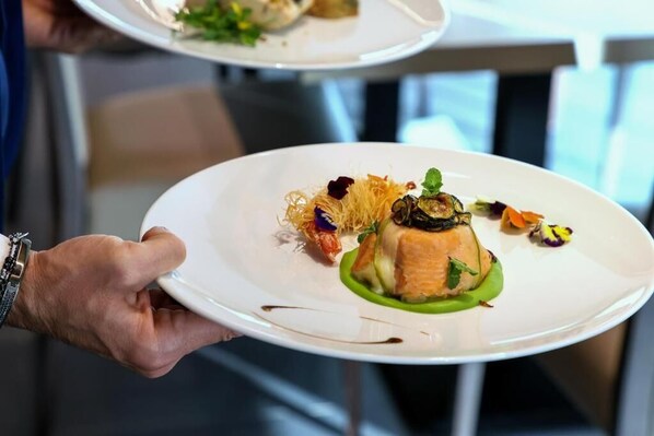 A person holding a white plate with a dish of salmon, greens, and decorative elements. - Hotel I Gigli (Nola)