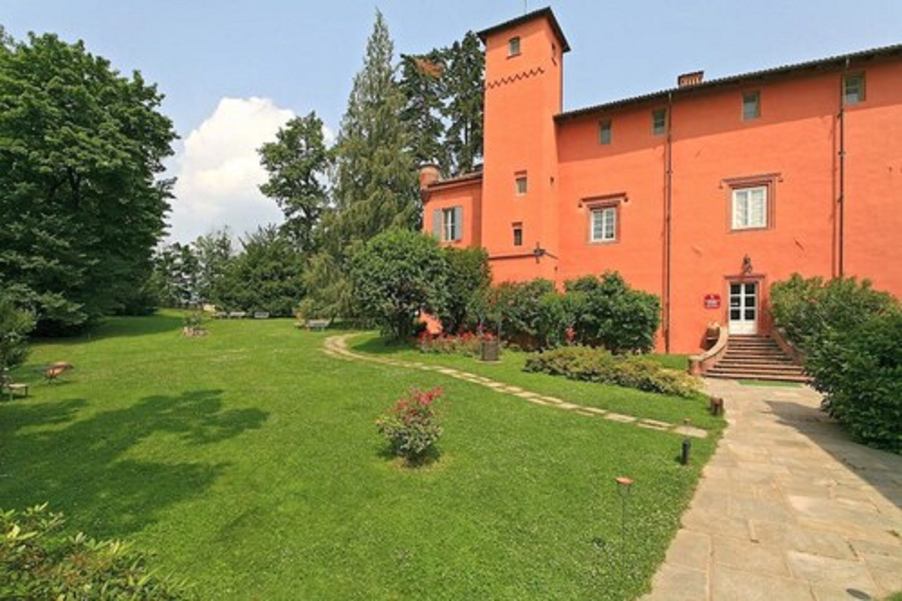 Un bâtiment rouge surmonté d’une tour, entouré d’une pelouse bien entretenue et d’arbres.